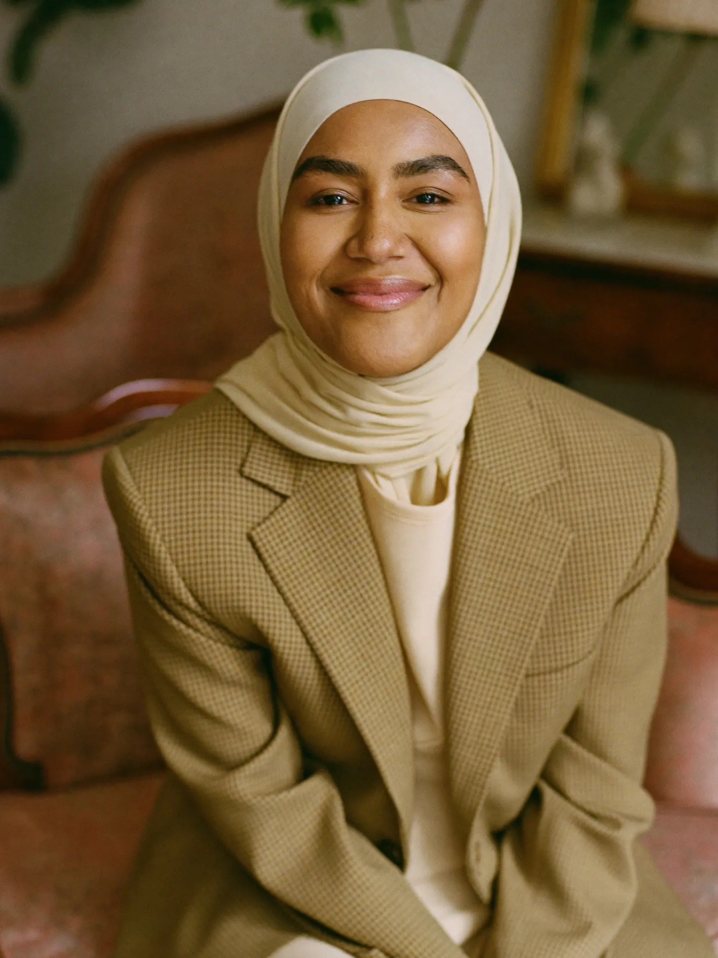 Perempuan berhijab dengan blazer kotak zaitun duduk di kursi tua
